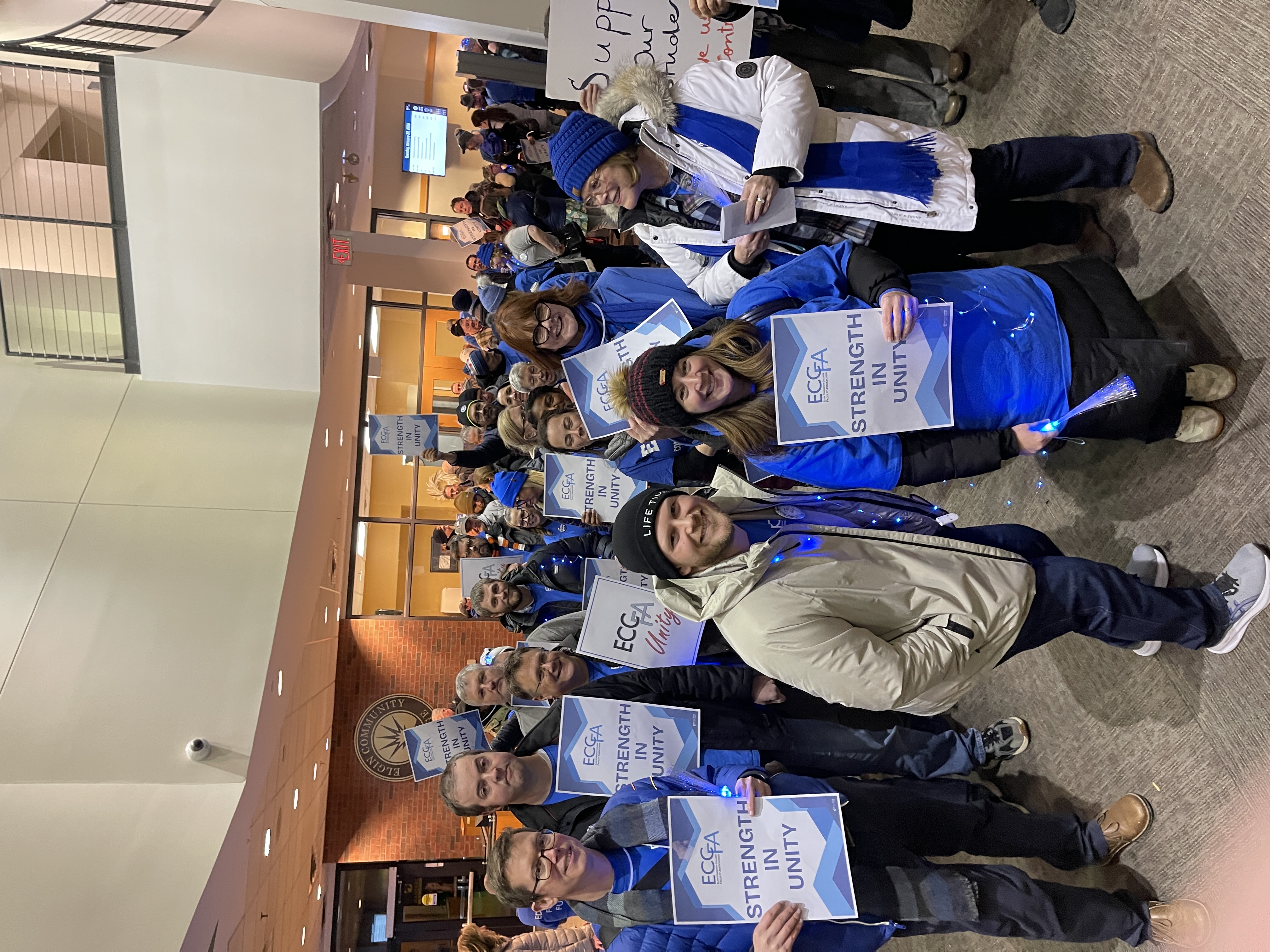 ECCFA members pose with their signs as they prepare to walk into a Board of Trustees meeting January 2026